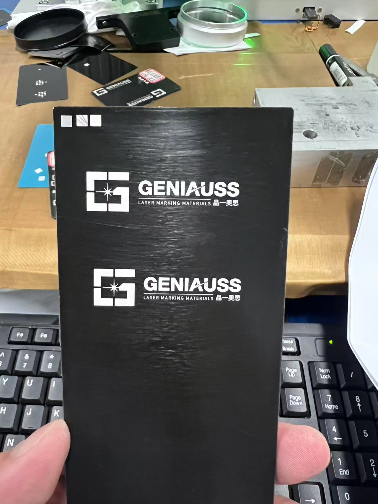 Black material sample with a bright white laser-marked logo on a metal laboratory marking bed